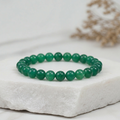Green beaded bracelet on a white stone surface with a blurred natural background